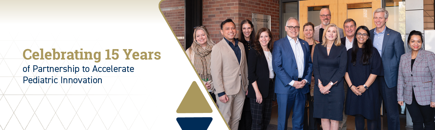 Group of people standing together outside a building next to a banner celebrating 15 years of partnership to accelerate pediatric innovation.