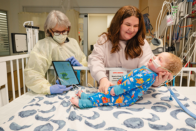 Jana Stockwell, M.D., shows a parent how the sensor‑filled fabric tracks pressure injury data and signals when a baby needs repositioning.